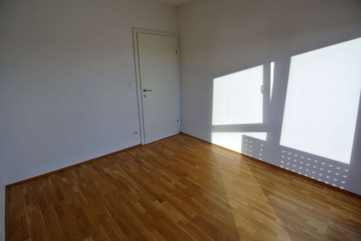 Leerer, heller Raum mit Parkettboden, weißen Wänden und Zimmertür
