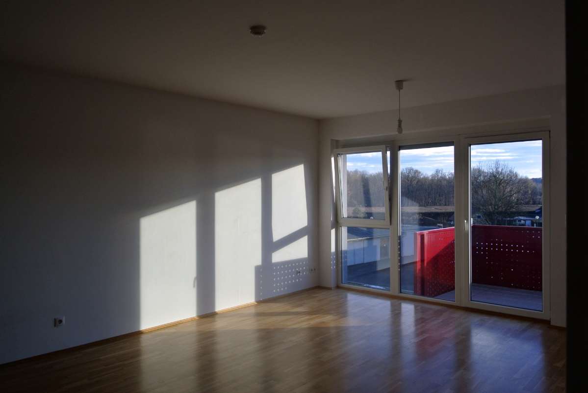 Helles Zimmer mit großem Fenster und Zugang zum Balkon mit rotem Geländer