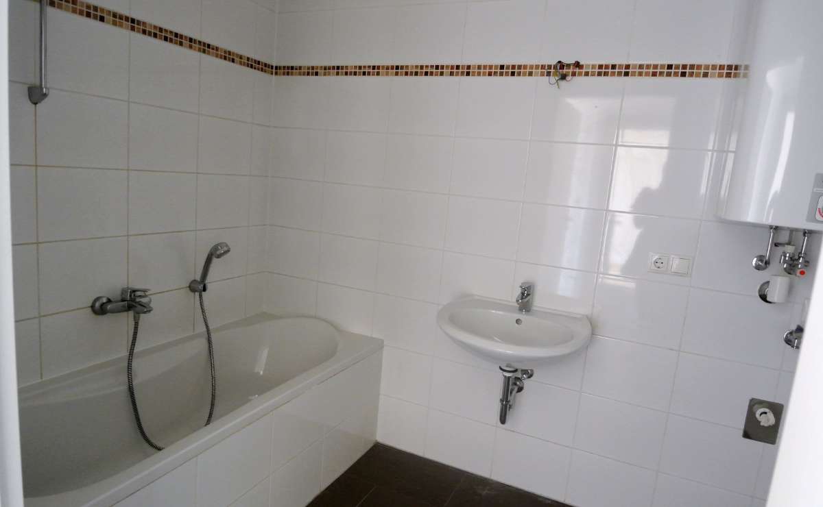 Badezimmer mit Badewanne, Waschbecken, Boiler und weißen Fliesenwänden