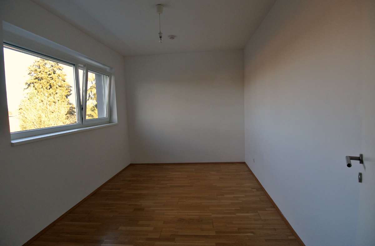 Einfaches Zimmer mit Holzboden, weiß gestrichenen Wänden und großem Fenster