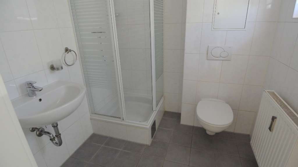 Kleines Badezimmer mit Dusche, Waschbecken, Wand-WC und weißen Fliesen