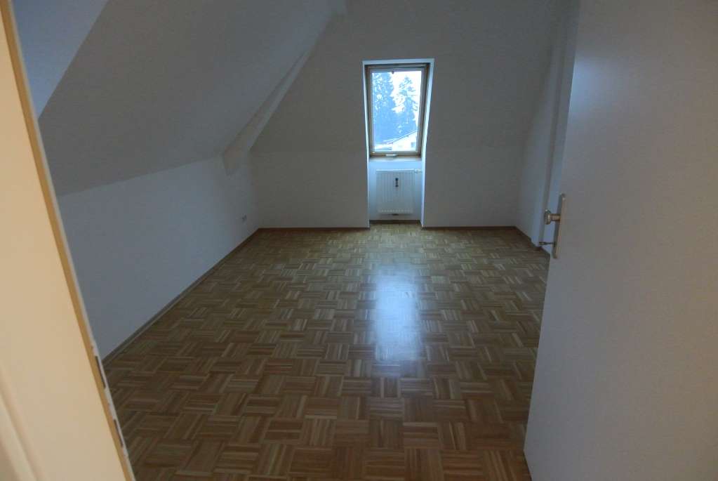 Zimmer mit Dachschräge, Parkettboden und kleinem Fenster über Heizkörper