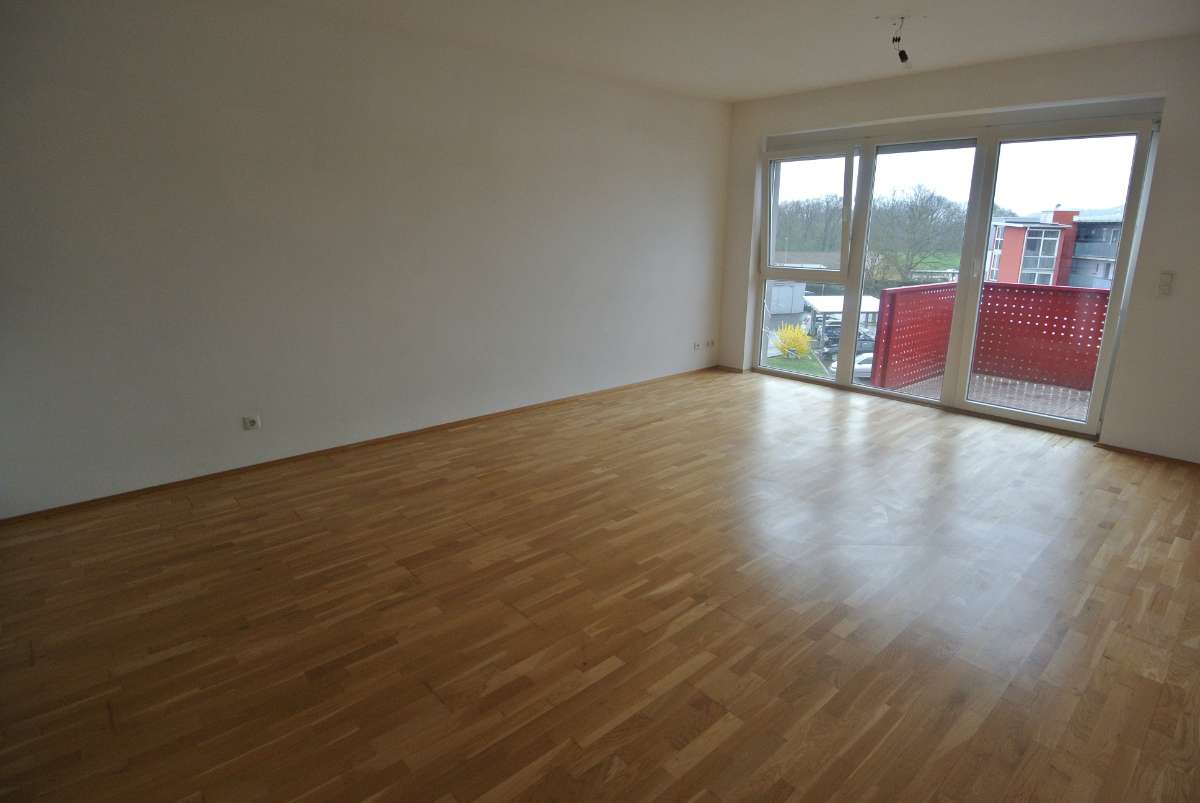 Leeres Wohnzimmer mit Parkettboden und großer Fensterfront zum Balkon