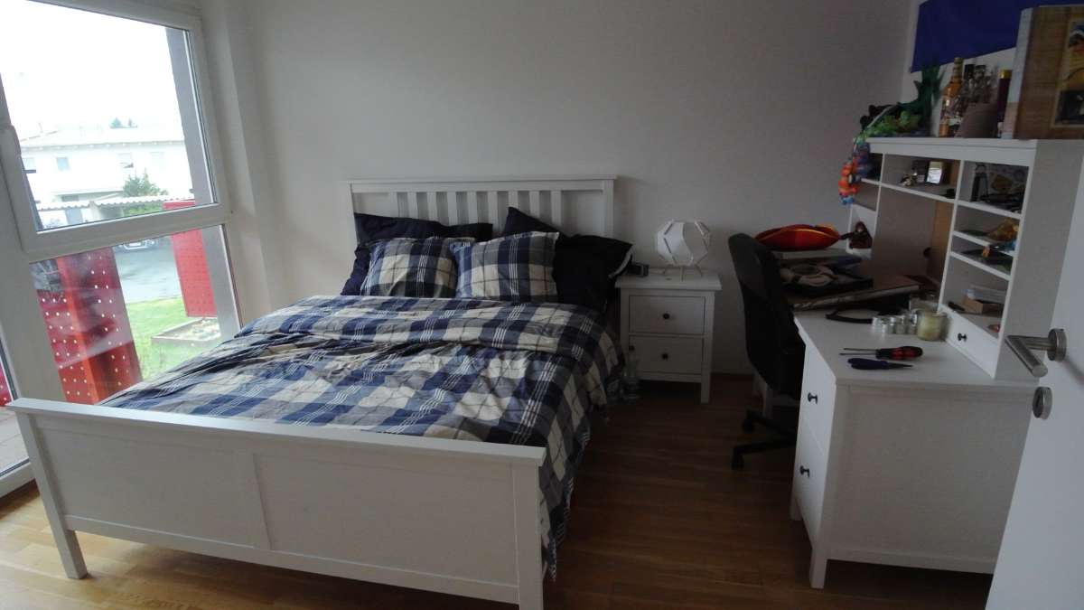 Schlafzimmer mit Bett, Schreibtisch und großem Fenster