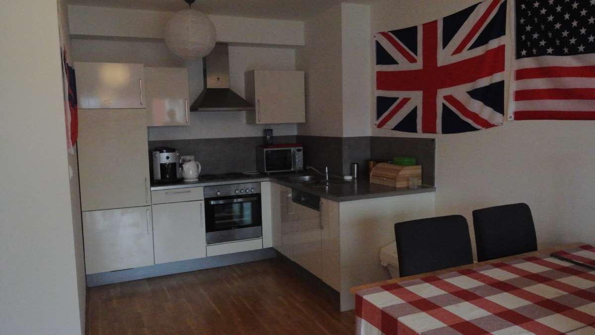 Kleine Küche mit heller Einbauzeile und Esstisch mit kariertem Tischtuch