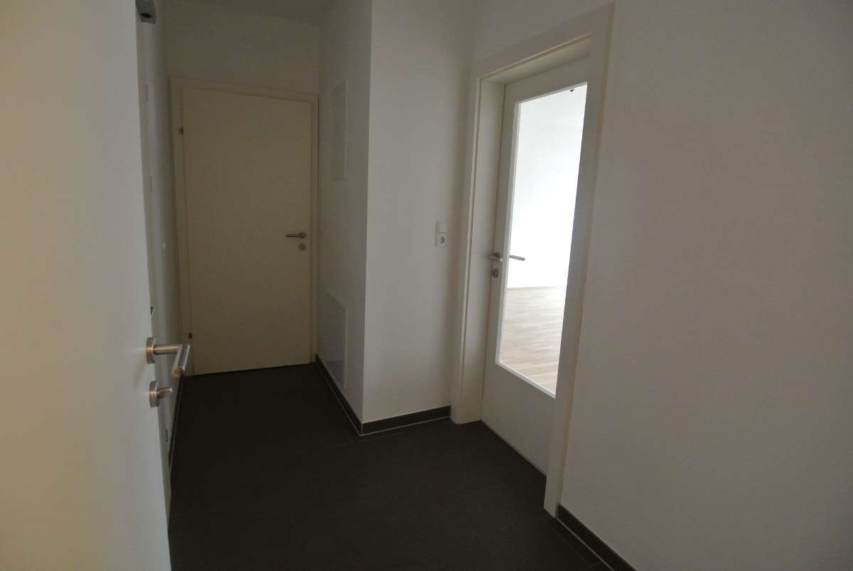 Schmaler Flur mit weiß gestrichenen Wänden und dunklem Fliesenboden