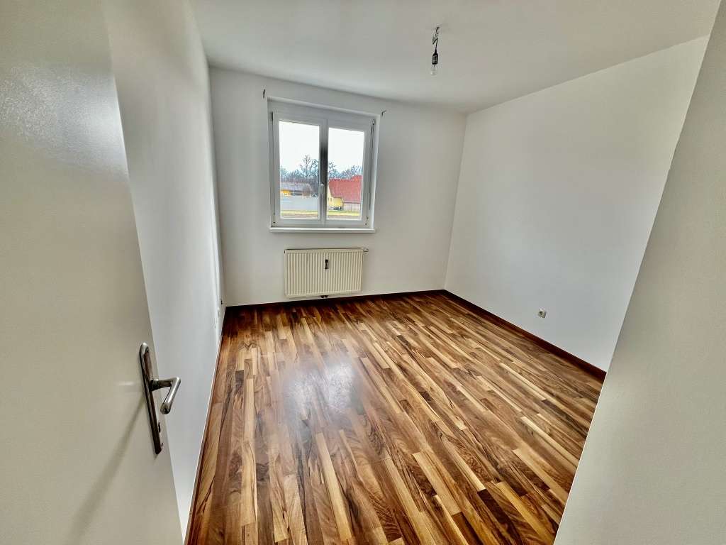 Helles Zimmer im Obergeschoss mit dunklem Holzlaminat und Fenster