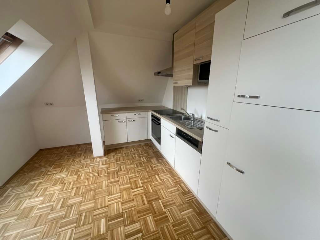 Kompakte Dachgeschossküche mit weißen Schränken, Herd und Dachflächenfenster