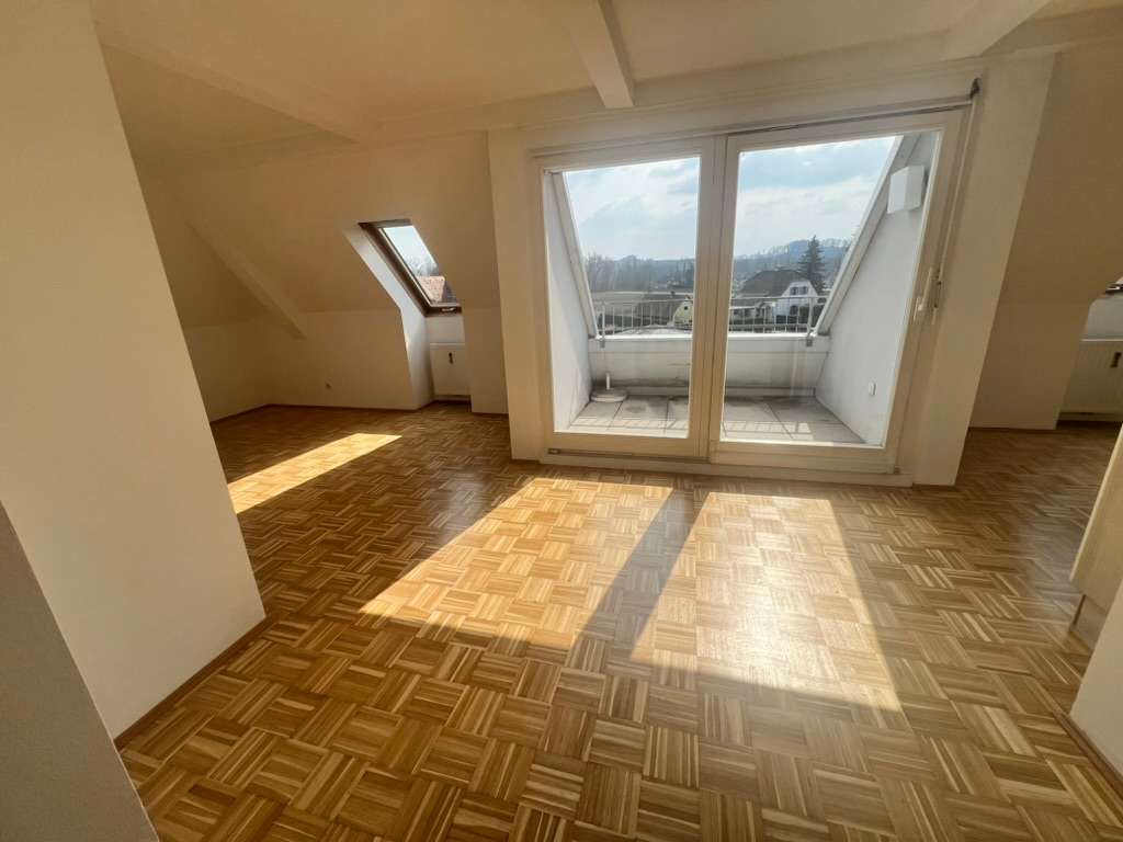 Großer, lichtdurchfluteter Dachgeschossraum mit Parkettboden und Zugang zu einem kleinen Balkon