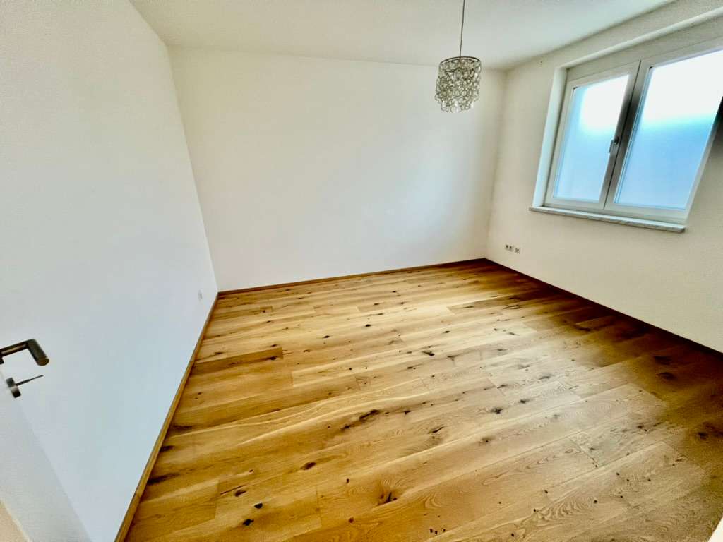 Leerer, heller Raum mit großem Fenster und Parkettboden