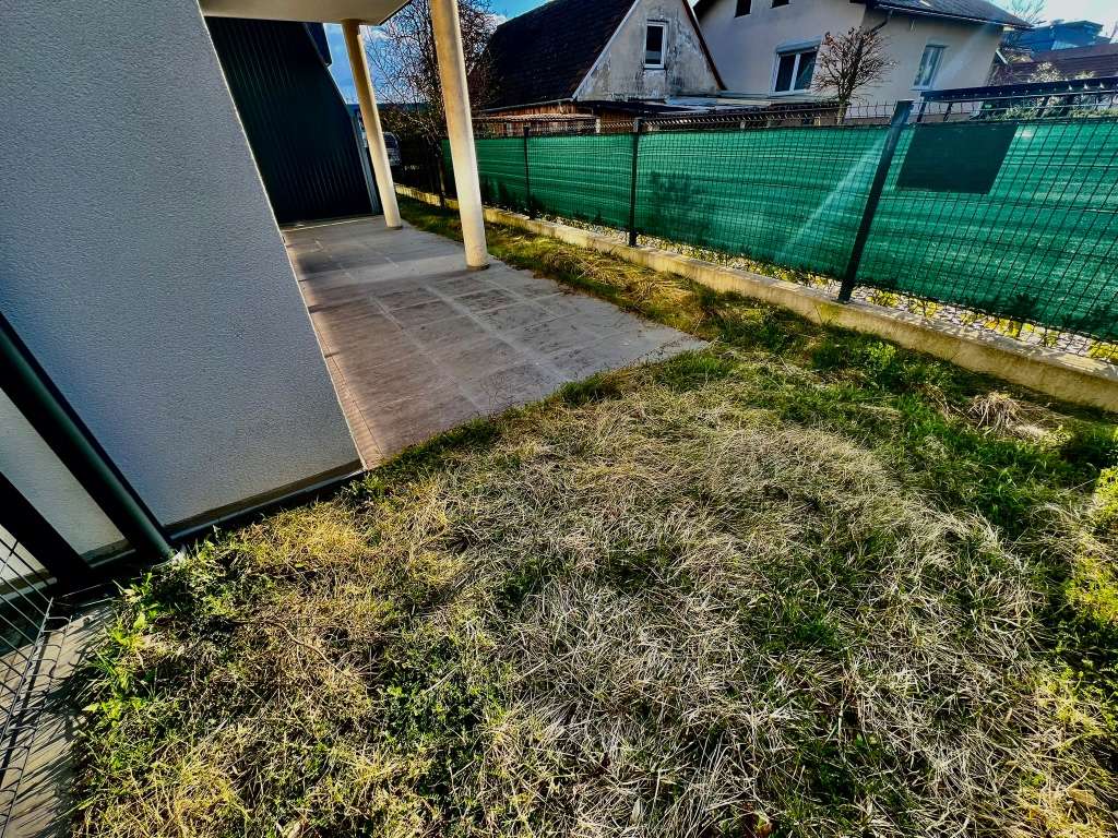 Kleiner Außenbereich mit betonierter Terrasse, Rasenstück und blickdichtem Zaun