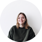 Smiling young woman with shoulder-length hair wearing a dark green sweater against a white background.