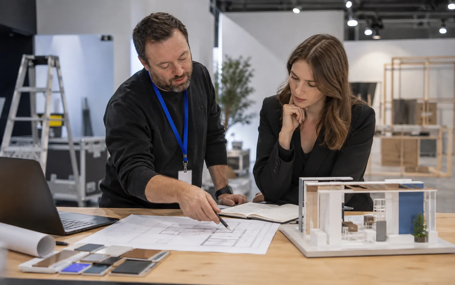 Generated scenario: A booth builder talks through a plain floorplan and a small physical architectural stand model with a marketing manager
