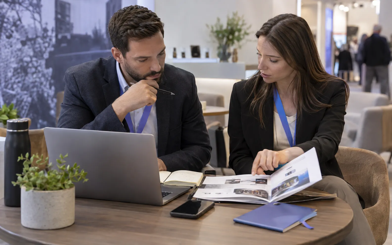 Generated scenario: A sales rep reviews a company dossier with role notes beside a laptop while a colleague points to a product brochure