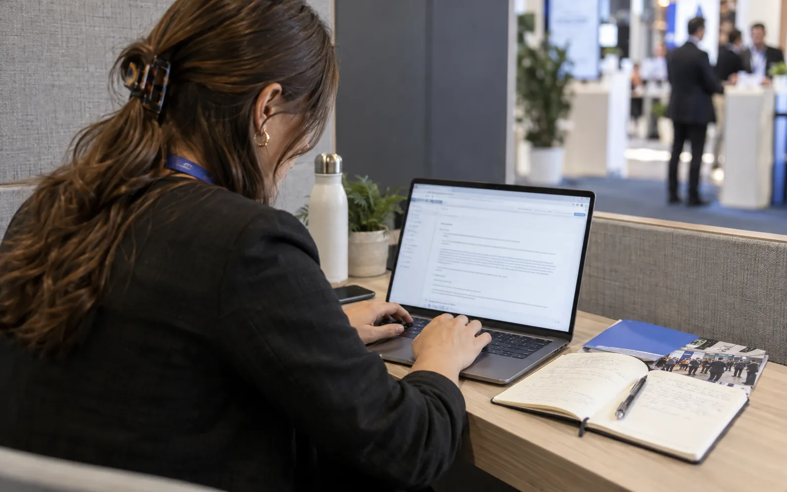 Generated scenario: A sales rep drafts a careful pre-show invitation at a laptop in a quiet booth alcove, consulting researched company notes and an event guide