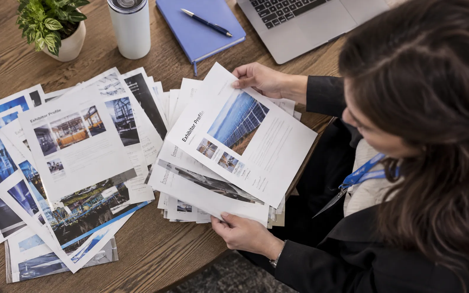 Generated scenario: A marketer sorts a broad pile of exhibitor profiles into a small relevant group at a table with product brochures