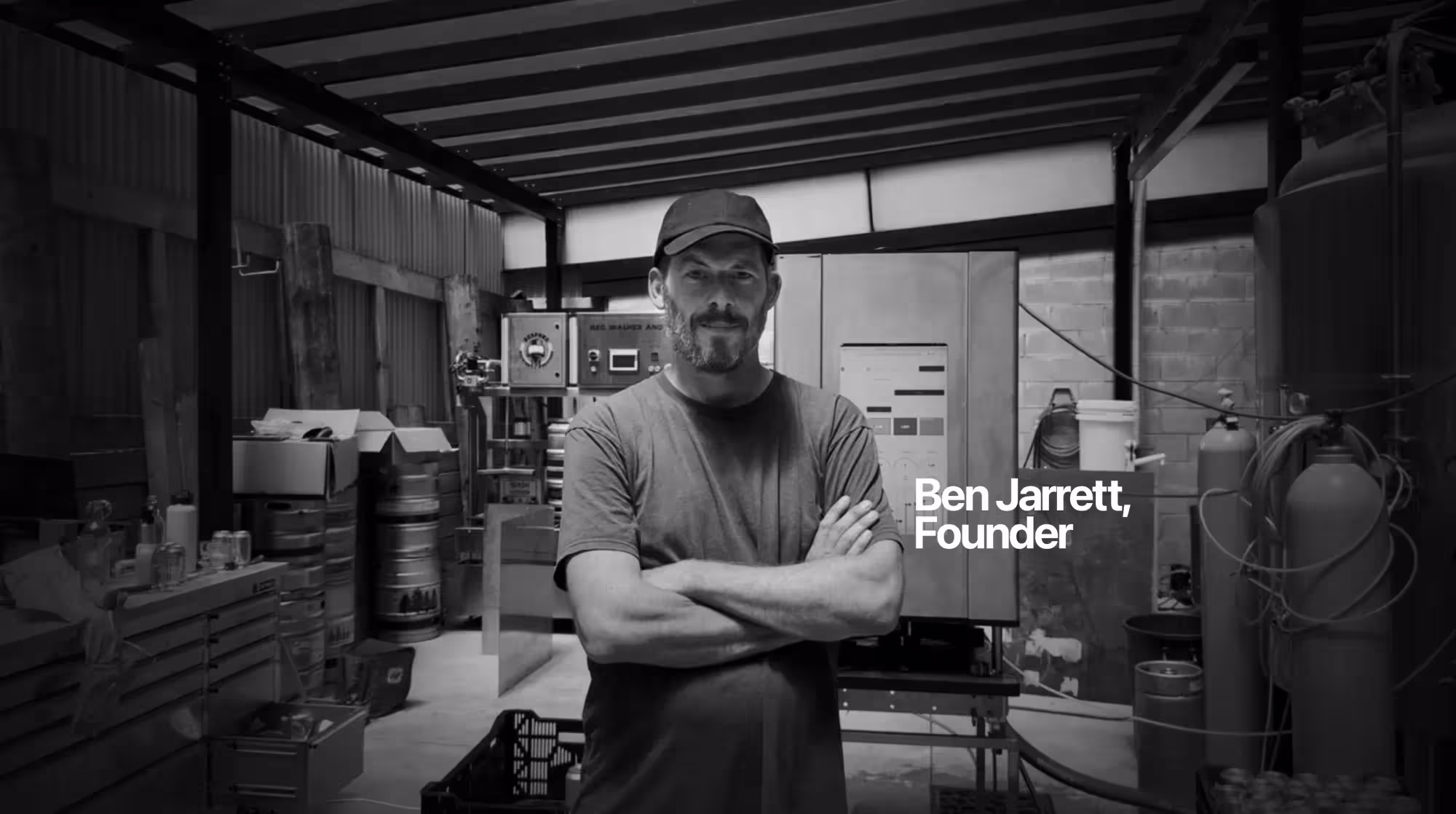 ZANZ founder Ben Jarrett standing with arms crossed in front of an early prototype canning machine in his garage workshop, where he spent five years developing the ZANZ autonomous canning machine