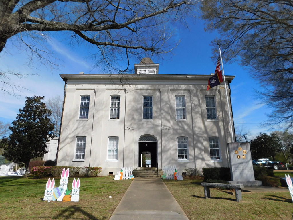 Historic two-story white courthouse building with American and state flags and Easter bunny decorations on the lawn.