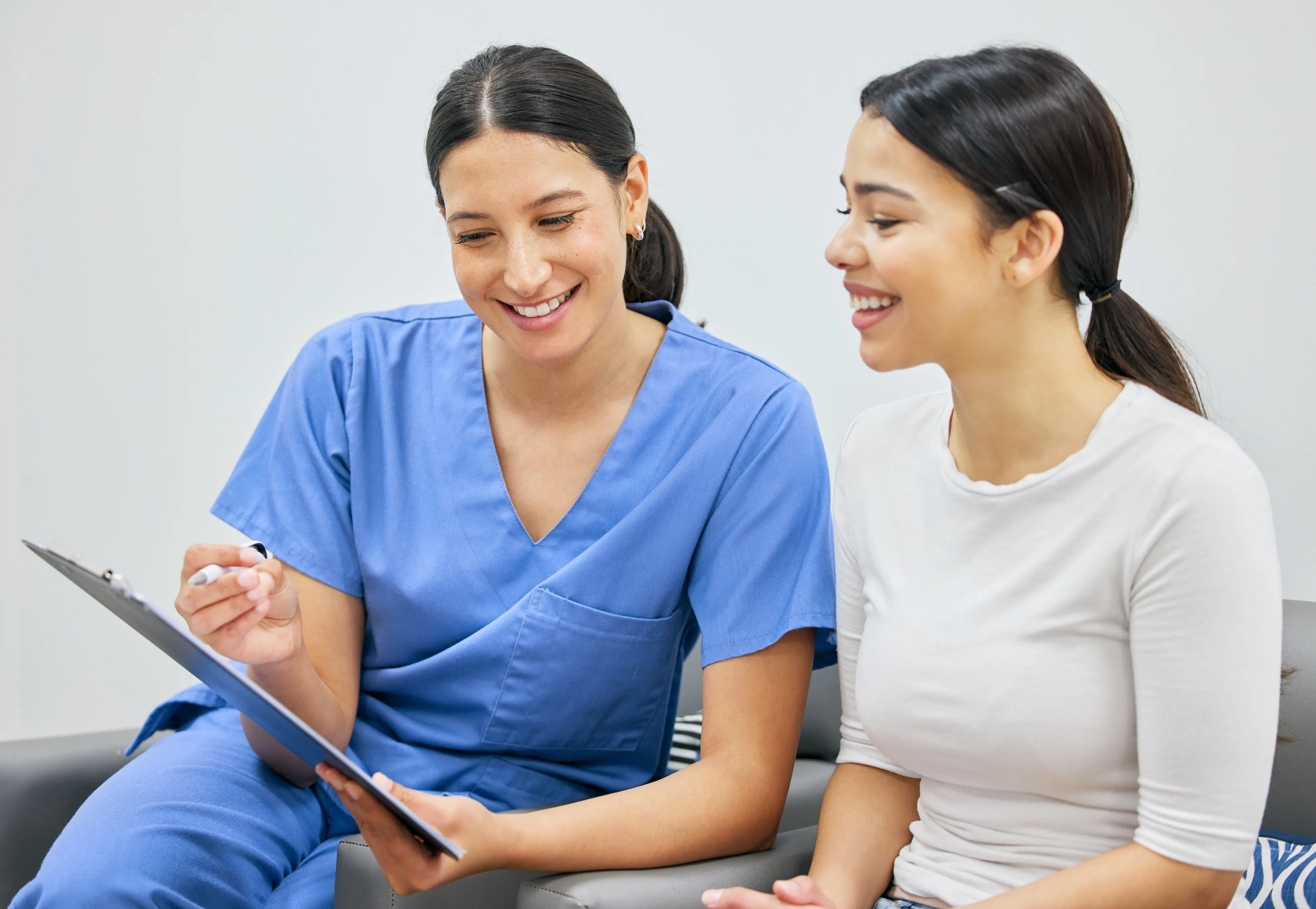 Female healthcare professional in blue scrubs showing a clipboard to a smiling woman in a white shirt at Azusa Dental Clinic