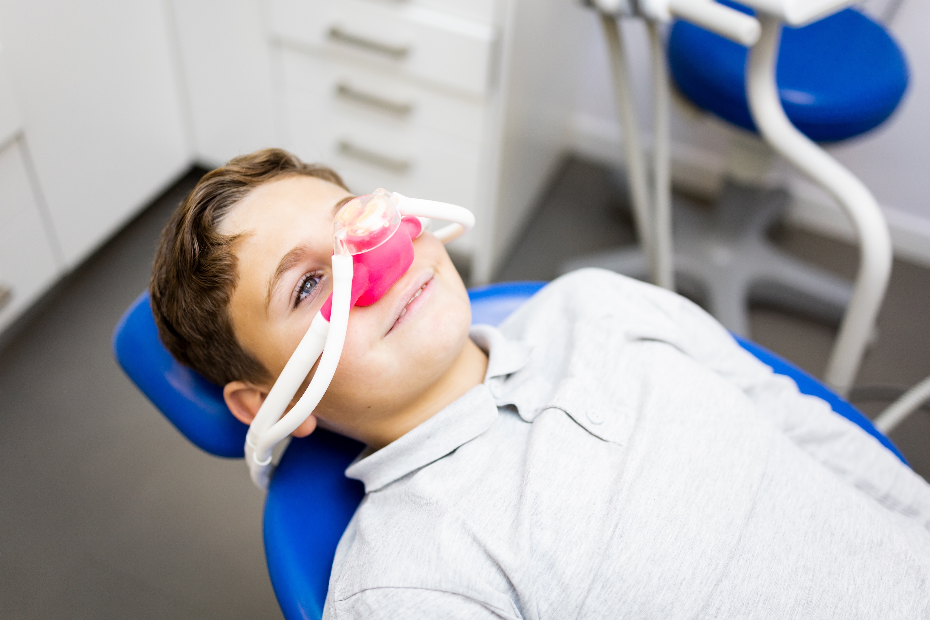 Young boy reclining in a dental chair wearing a pink and clear nasal mask for sedation