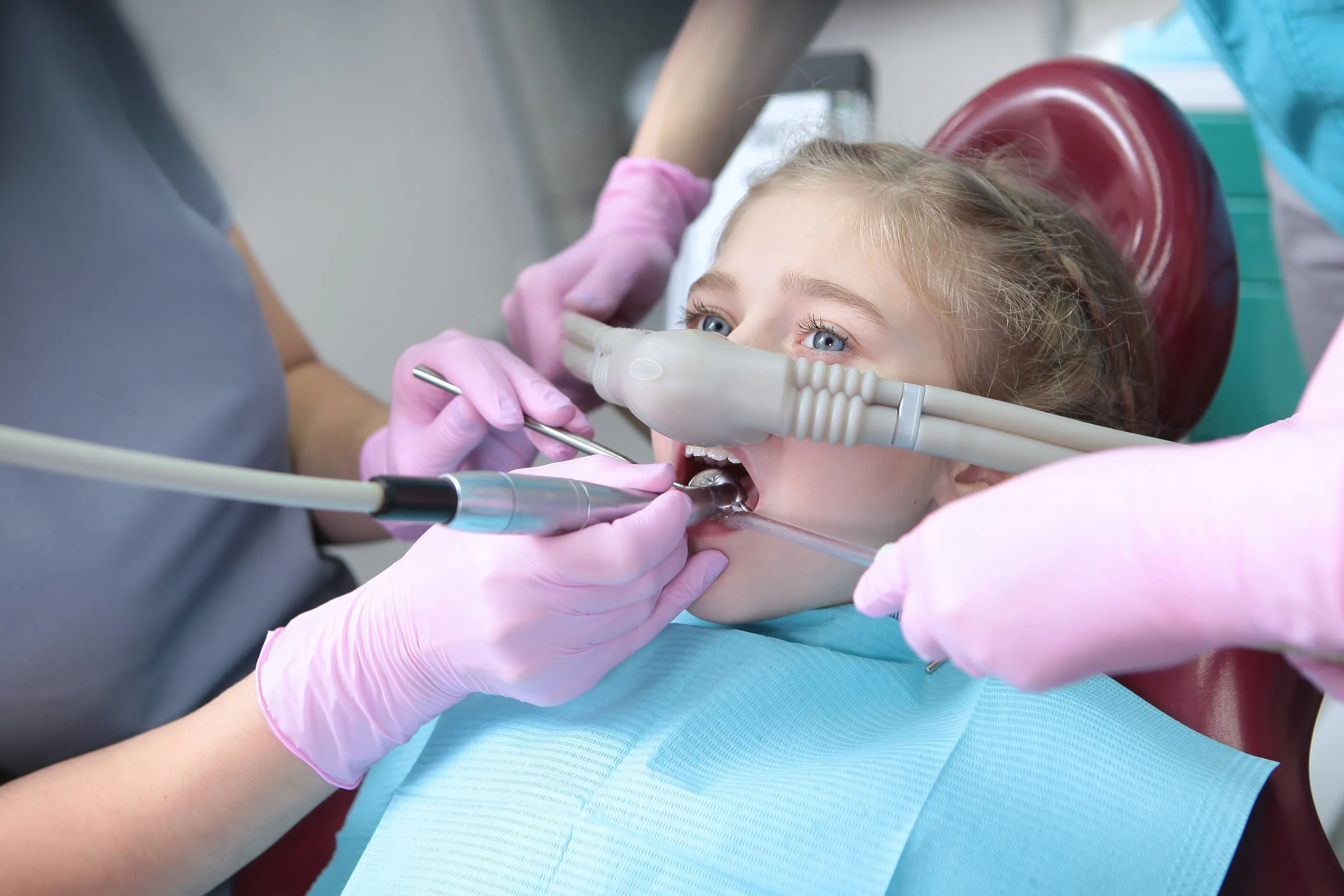 Young girl receiving dental treatment with dental tools and protective mouth device in a clinic.
