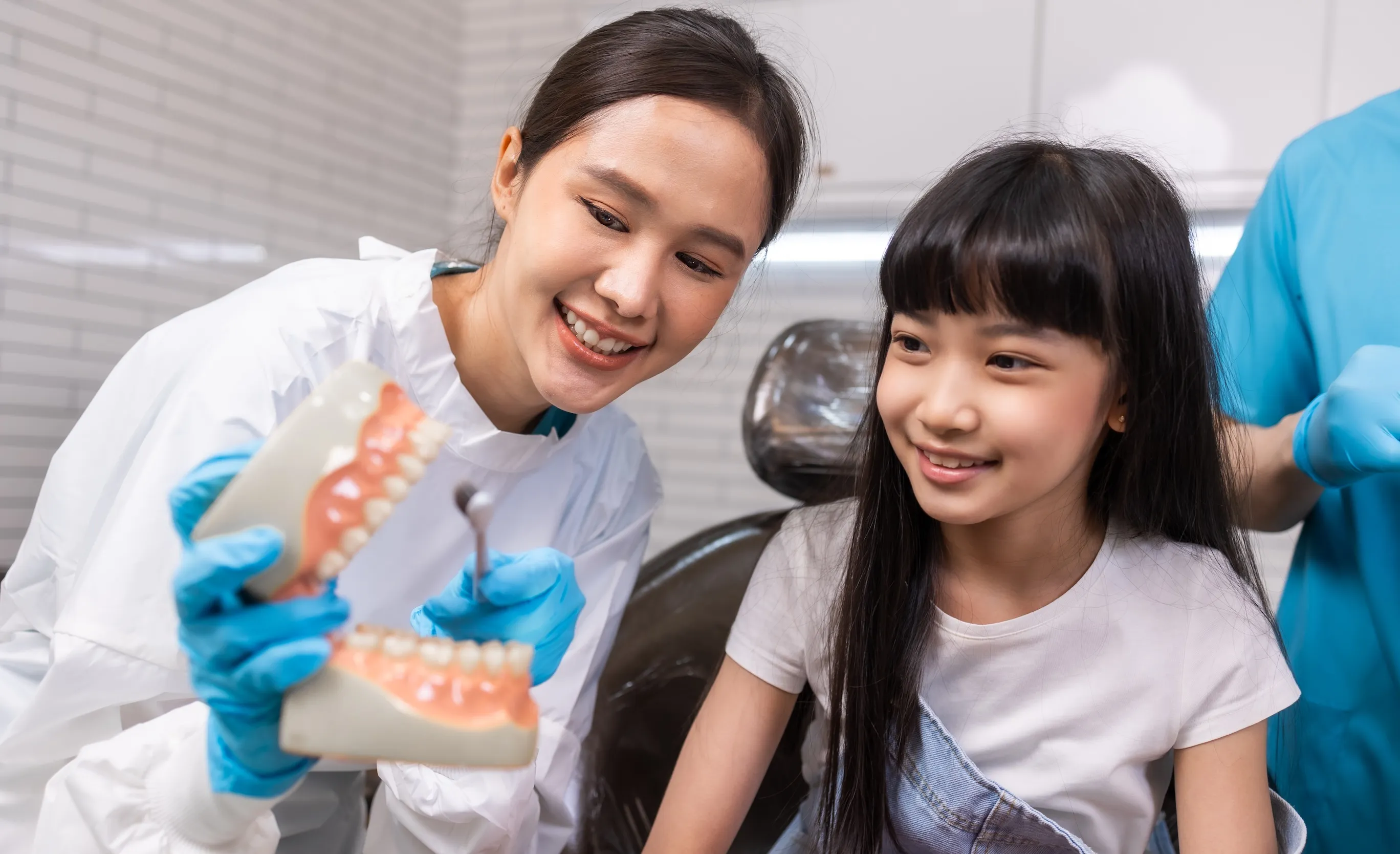 Female dentist wearing blue gloves showing a dental model to a smiling young girl in Azusa Dental Clinic