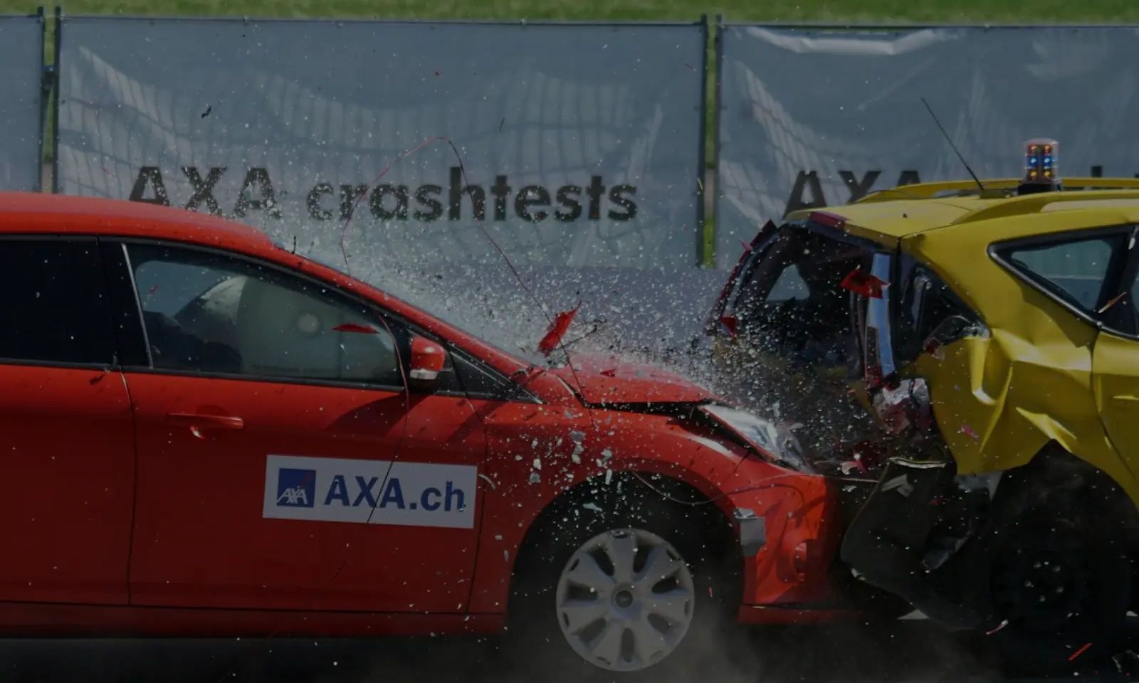 Red AXA.ch crash test car colliding into the rear of a yellow test vehicle with debris and glass flying.