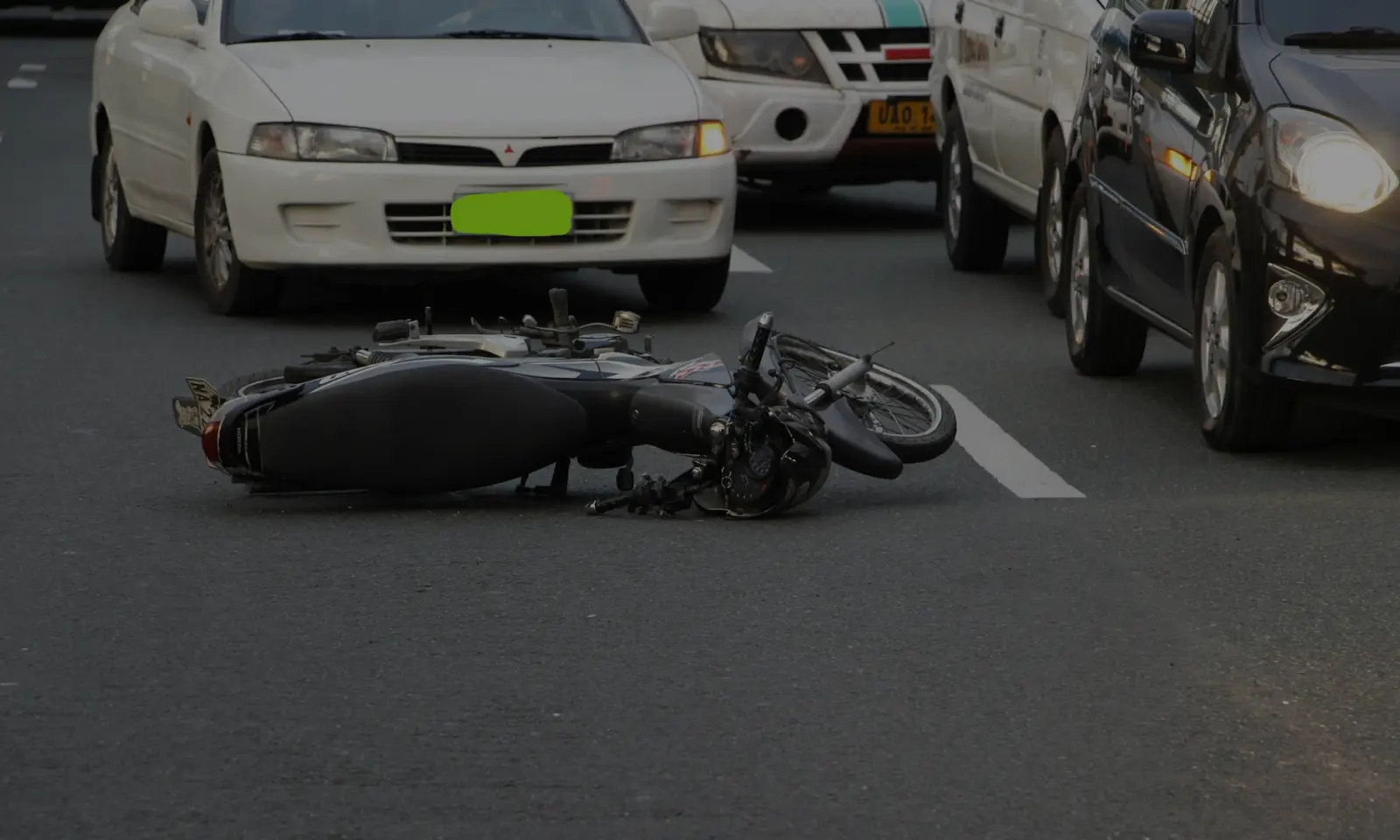 Motorcycle lying on its side in the middle of a road with cars stopped behind it.
