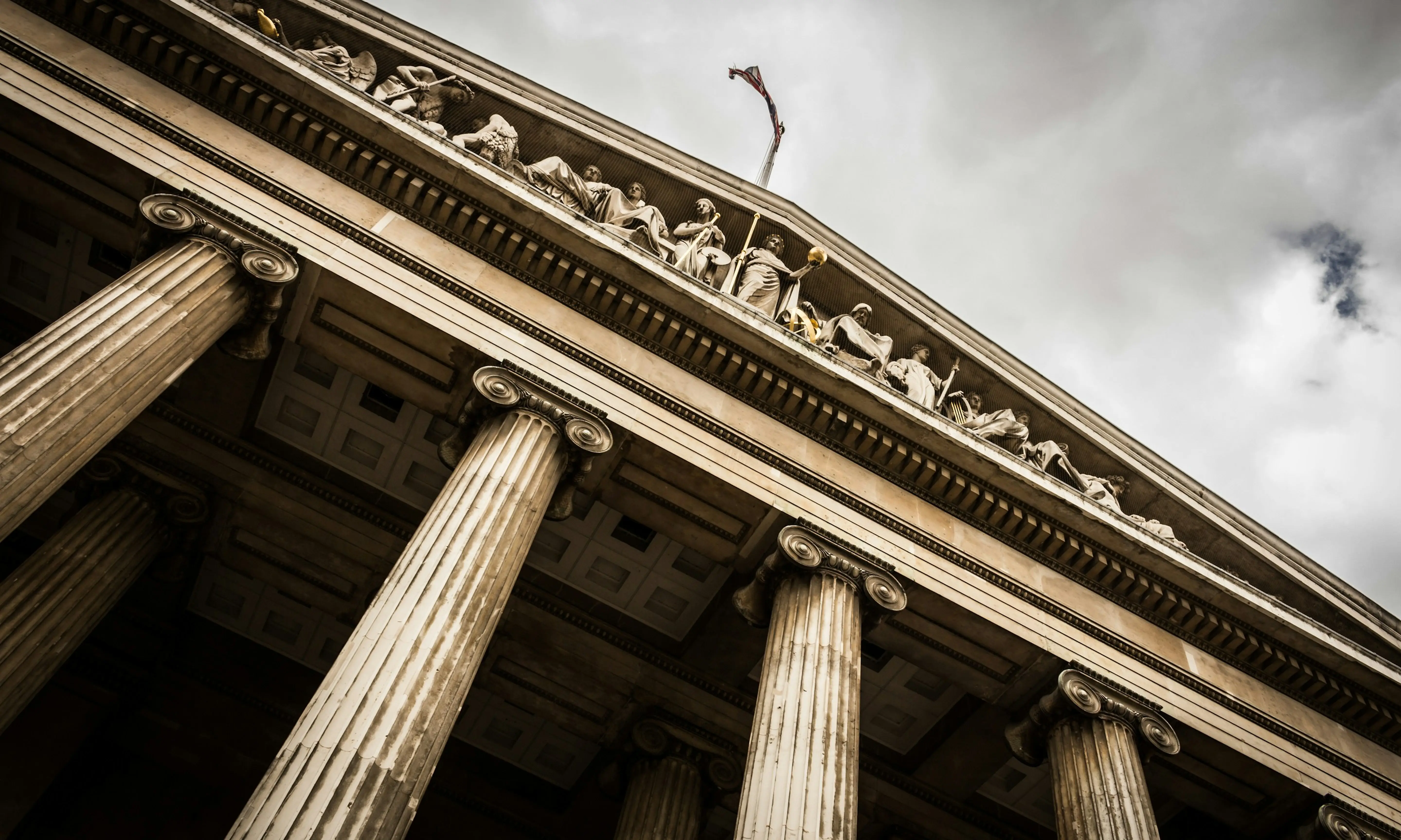Low-angle view of a classical building facade with tall Corinthian columns and sculpted figures under its triangular pediment.