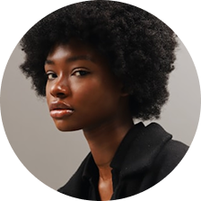 Portrait of a young Black woman with natural afro hairstyle wearing a black top against a neutral background.