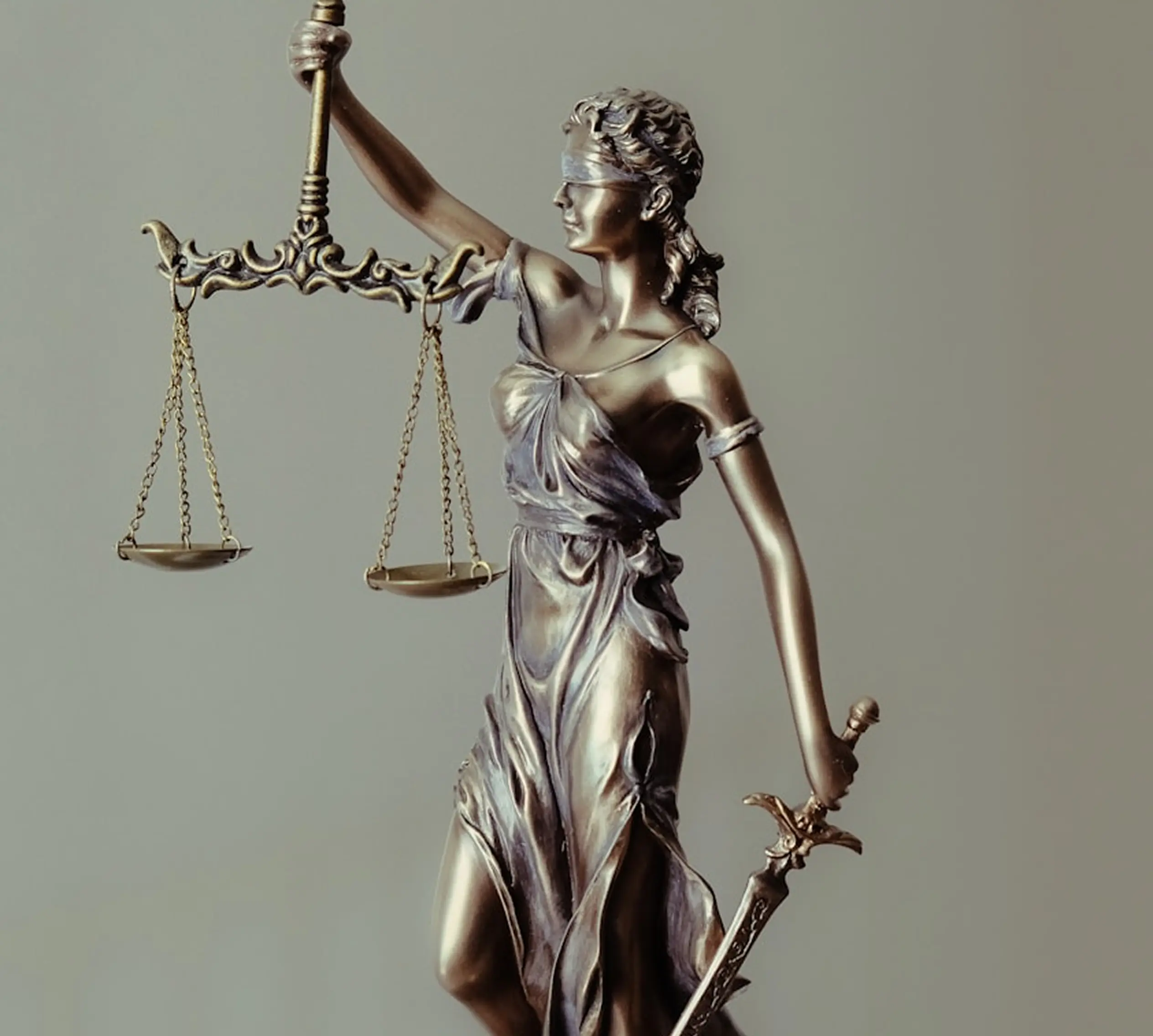 Bronze statue of Lady Justice holding scales in one hand and a sword in the other, blindfolded against a plain background.
