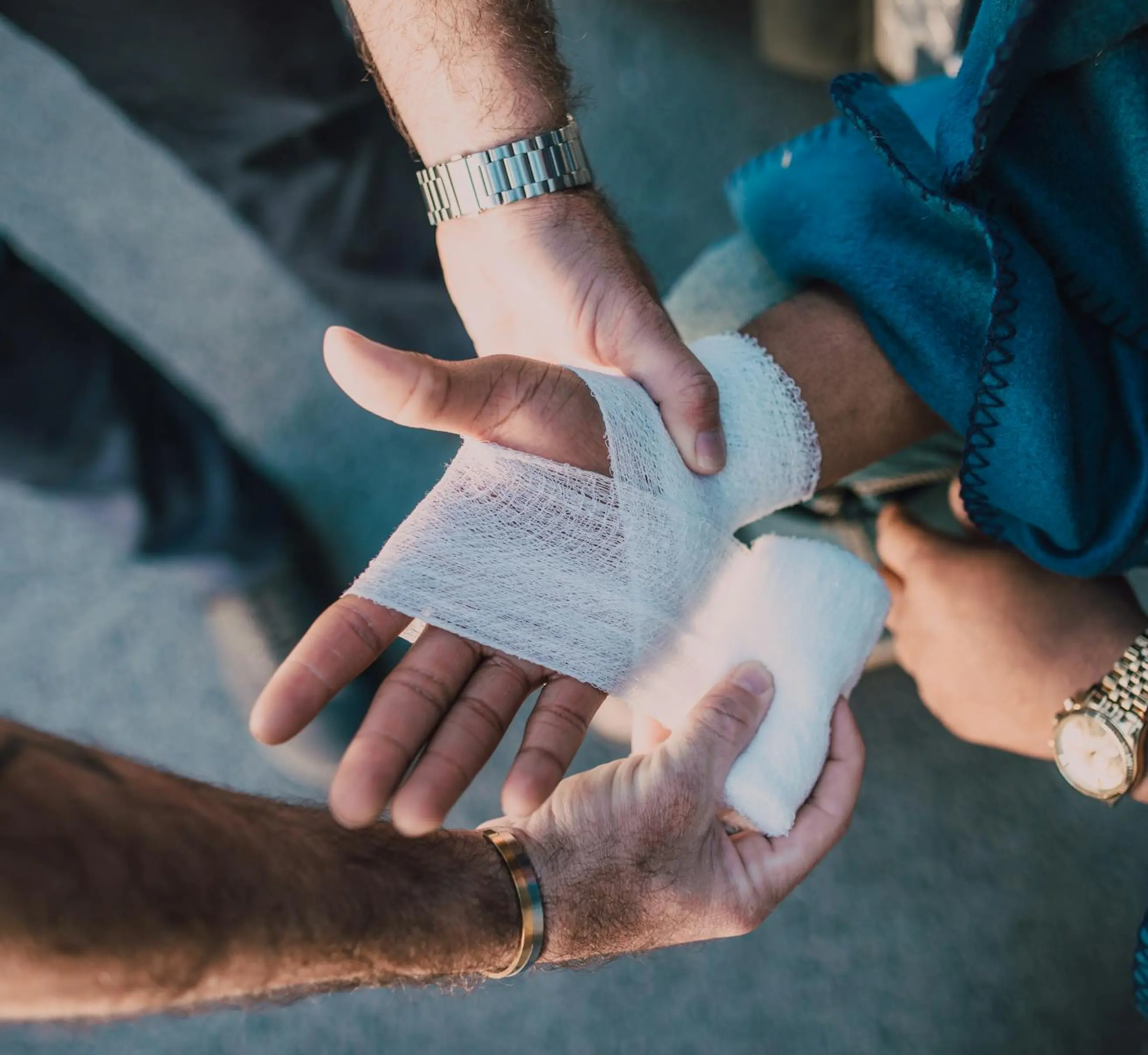 Person wrapping a white gauze bandage around another person's injured hand.