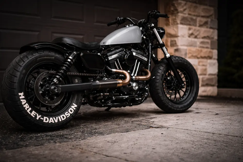 Custom Harley-Davidson motorcycle with white tire lettering on rear wheel, parked in front of a garage.