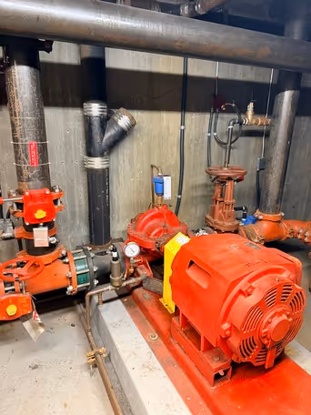 Red industrial pump system with connected black pipes and pressure gauge on concrete floor.