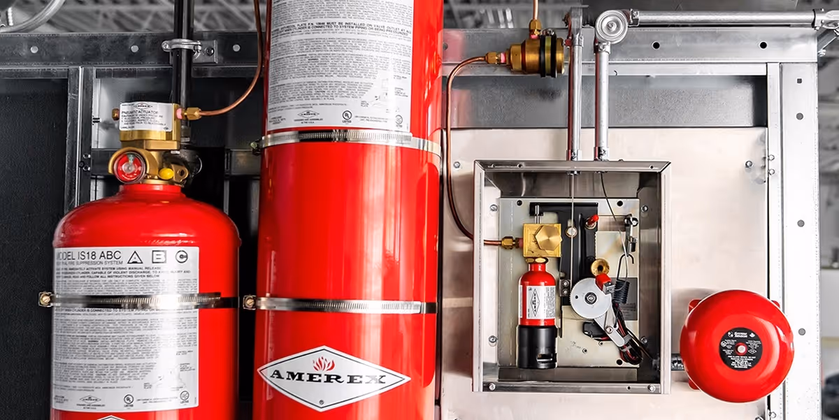 Close-up of a red Amerex fire suppression system with cylinders and control panel mounted on a metal frame.