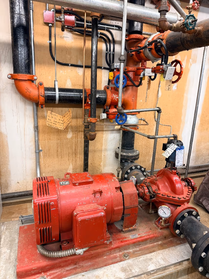 Red industrial pump unit with connected black pipes and blue valve handles mounted on a concrete floor.