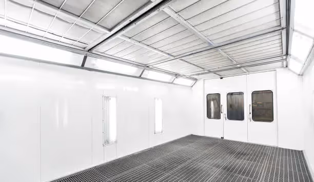 Empty industrial paint booth with white walls, grated floor, and closed doors with windows.