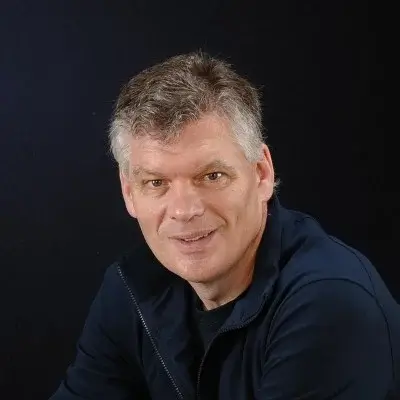 Portrait of a middle-aged man with gray hair wearing a dark blue jacket against a black background