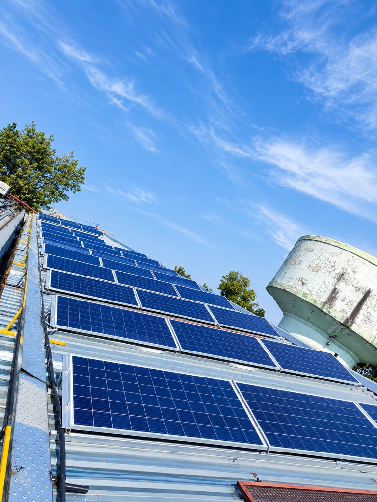 Solar panels on a sloping factory roof under a bright sky