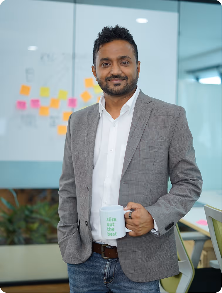 Man in gray blazer and white shirt holding a white mug labeled 'slice out the best' in an office with sticky notes on a glass wall.