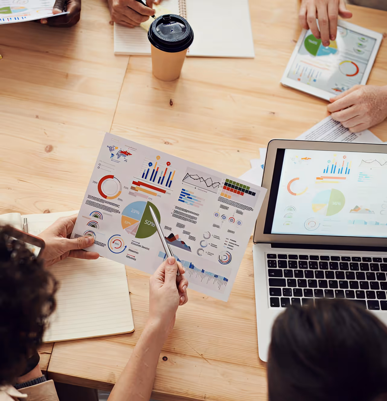 People reviewing printed and digital charts with graphs, pie charts, and data visualizations on a wooden table.