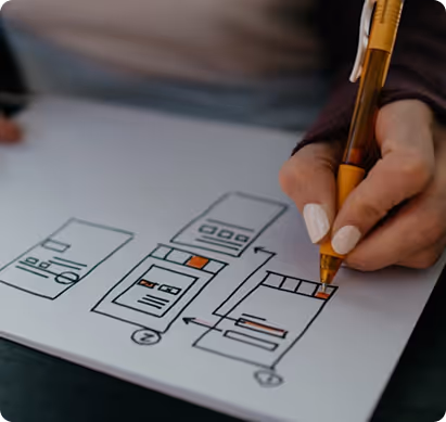 Hand holding a pen sketching a wireframe layout of a mobile app on white paper.