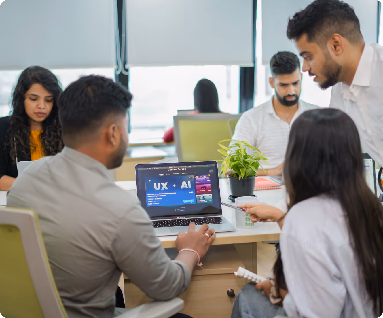 Group of people collaborating around a table with a laptop displaying a UX + AI course webpage.