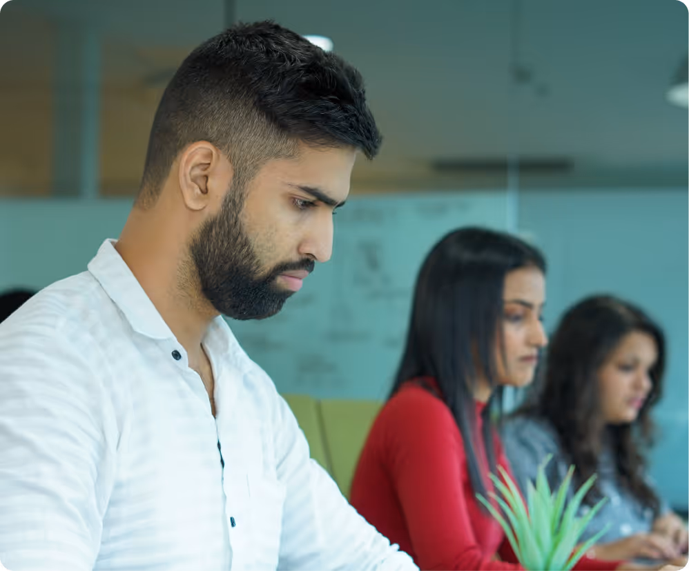Man in white shirt focused on work with two women working in the background in an office setting.