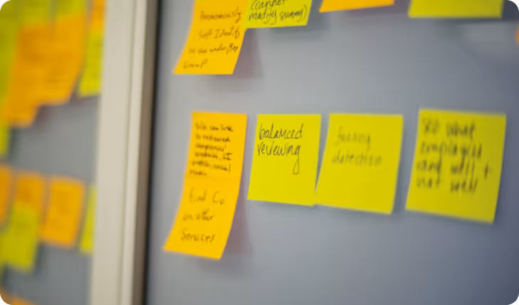 Yellow sticky notes with handwritten text, including 'balanced reviewing', attached to a gray glass board.