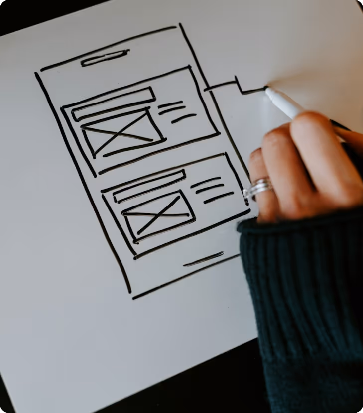 Hand sketching a website wireframe layout with two content blocks on white paper using a black marker.