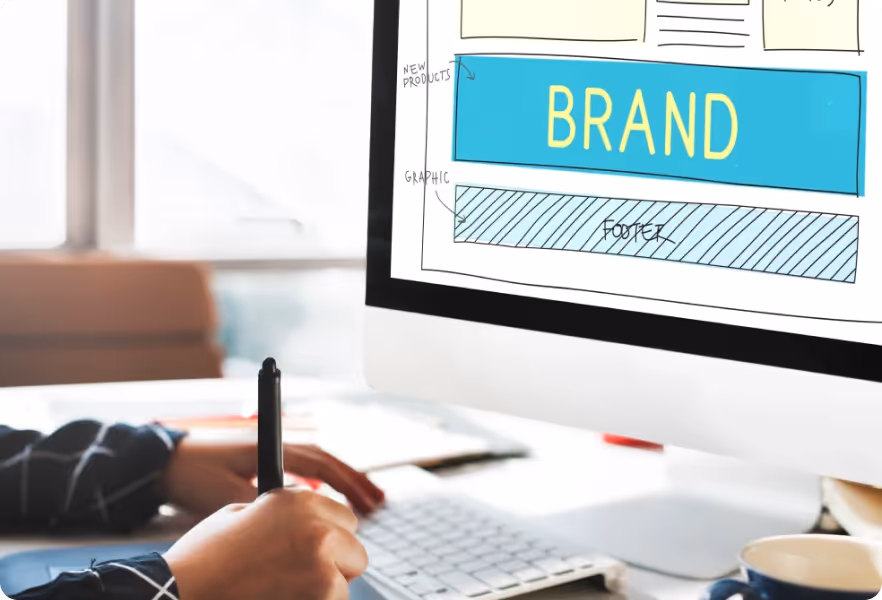 Person sketching website design layout with labeled sections including brand, new products, graphic, and footer on a computer screen.