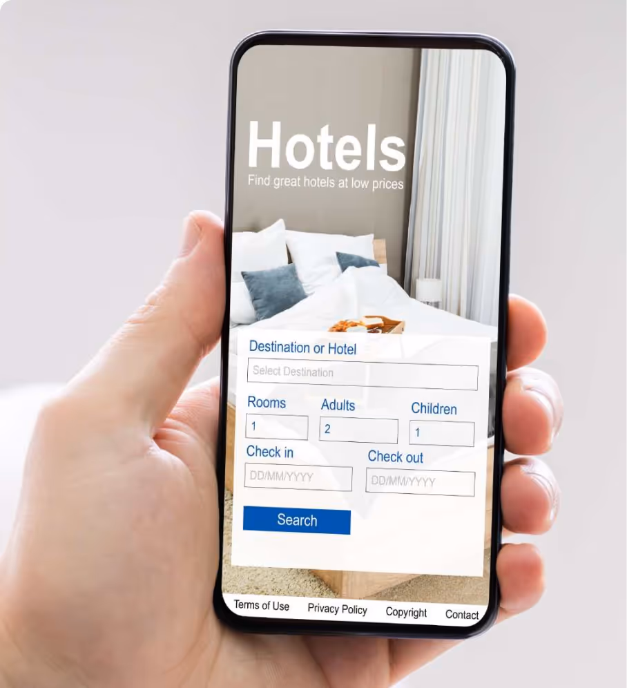 Hand holding smartphone showing a hotel booking app with fields for destination, rooms, adults, children, check-in and check-out dates, and a search button.