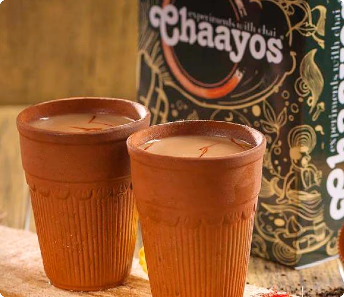 Two traditional clay cups filled with chai tea, with a chaiyos branded package in the background.