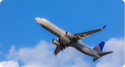 Commercial airplane with a blue tail flying upwards against a blue sky with scattered clouds.